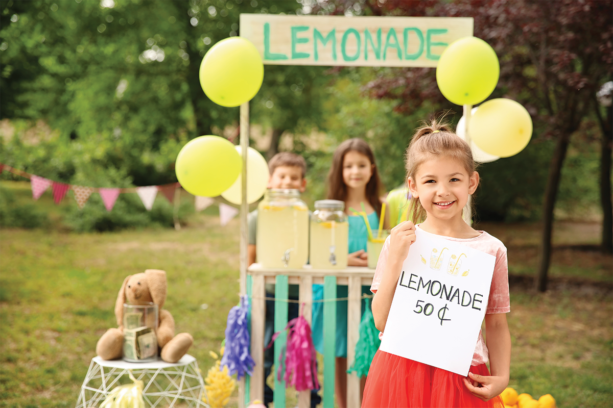 A young girl and her friends putting on a lemon aid stand for a fun summer activity. 