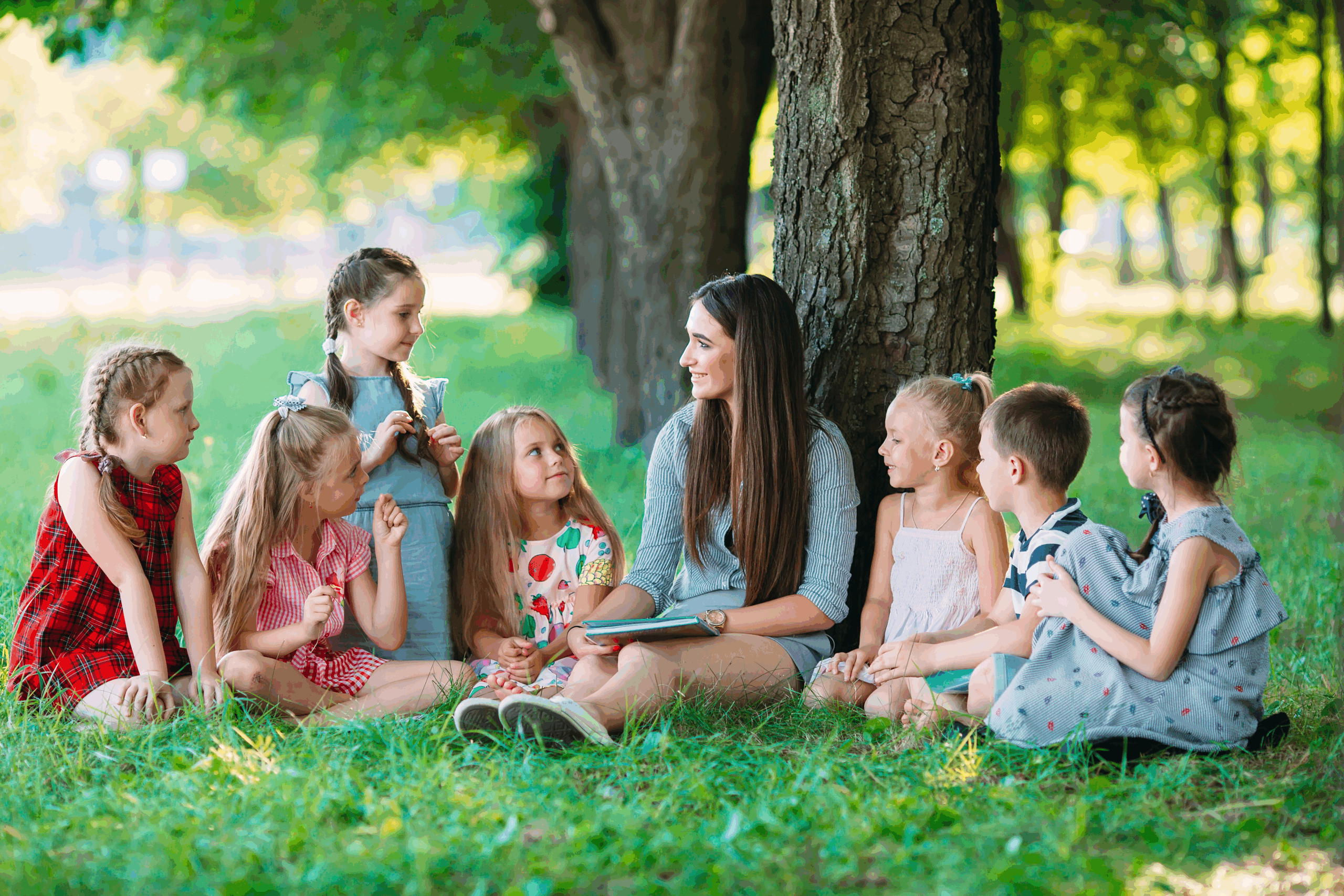 A group of children sitting outside under a tree enjoying a fun summer story time. 