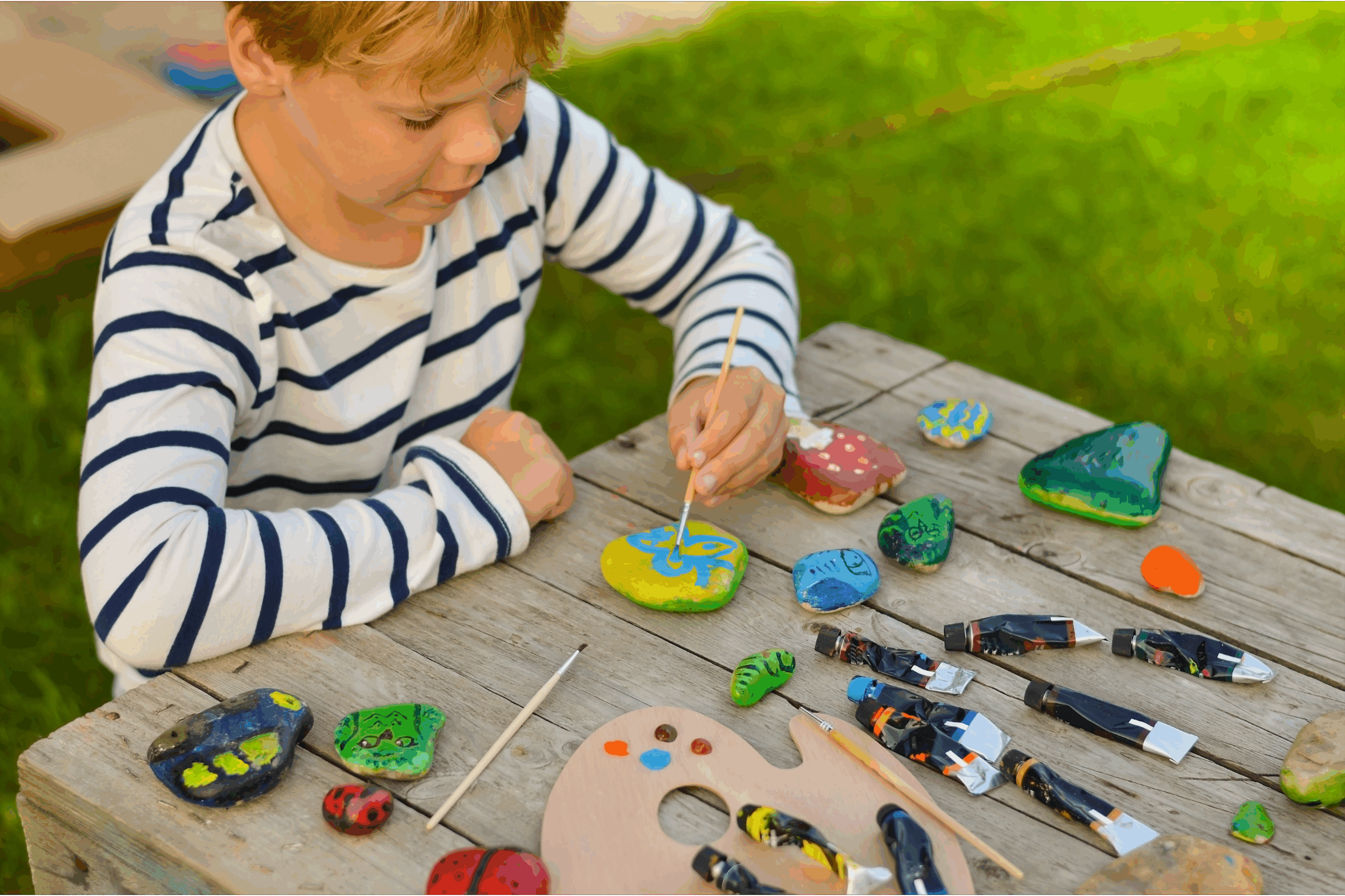 A boy painting rocks bright and colorful for a fun summer activity for kids.