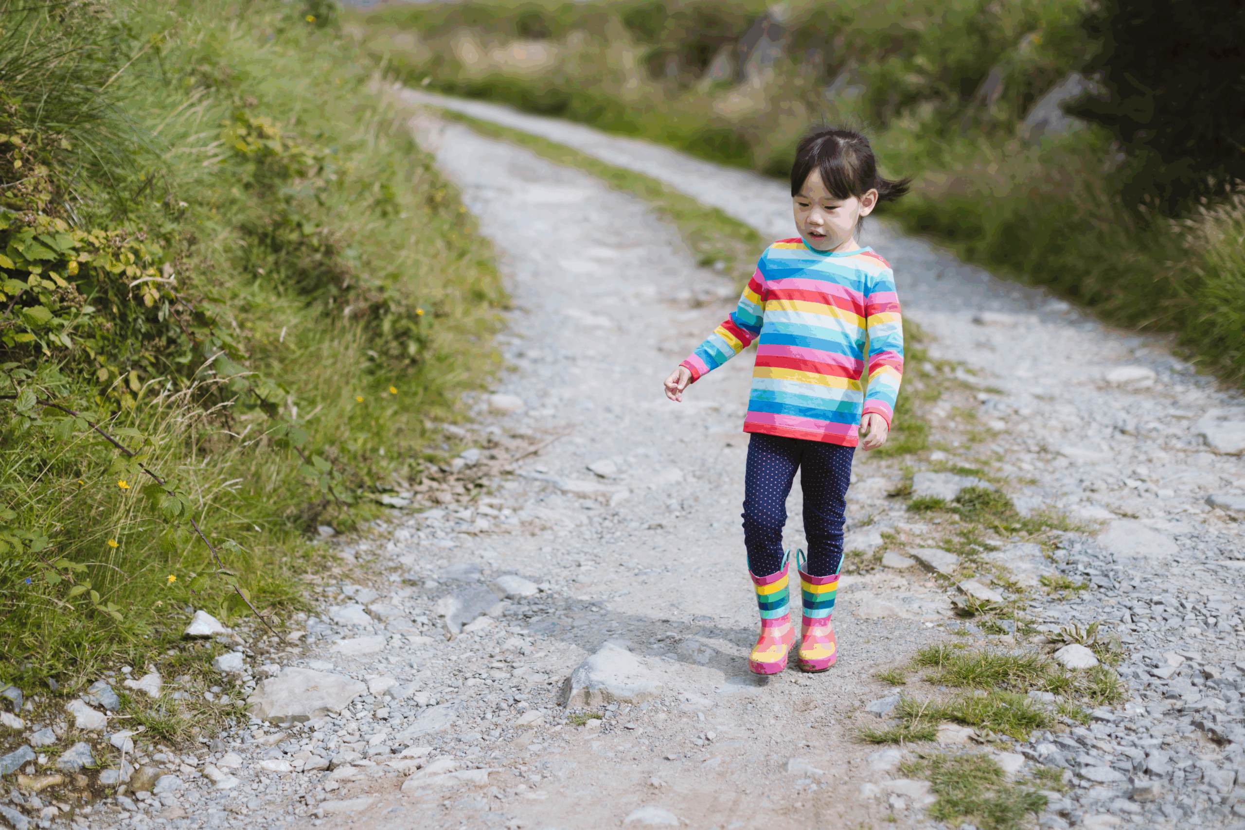 A young child walking down a gravel road out in nature. 