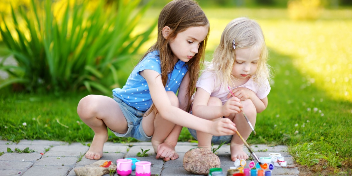 Two young girls enjoying a summer craft of painting outside.