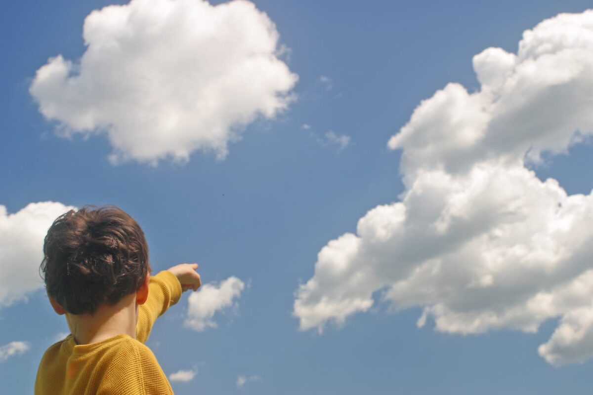 A young boy pointing at clouds in the sky. 