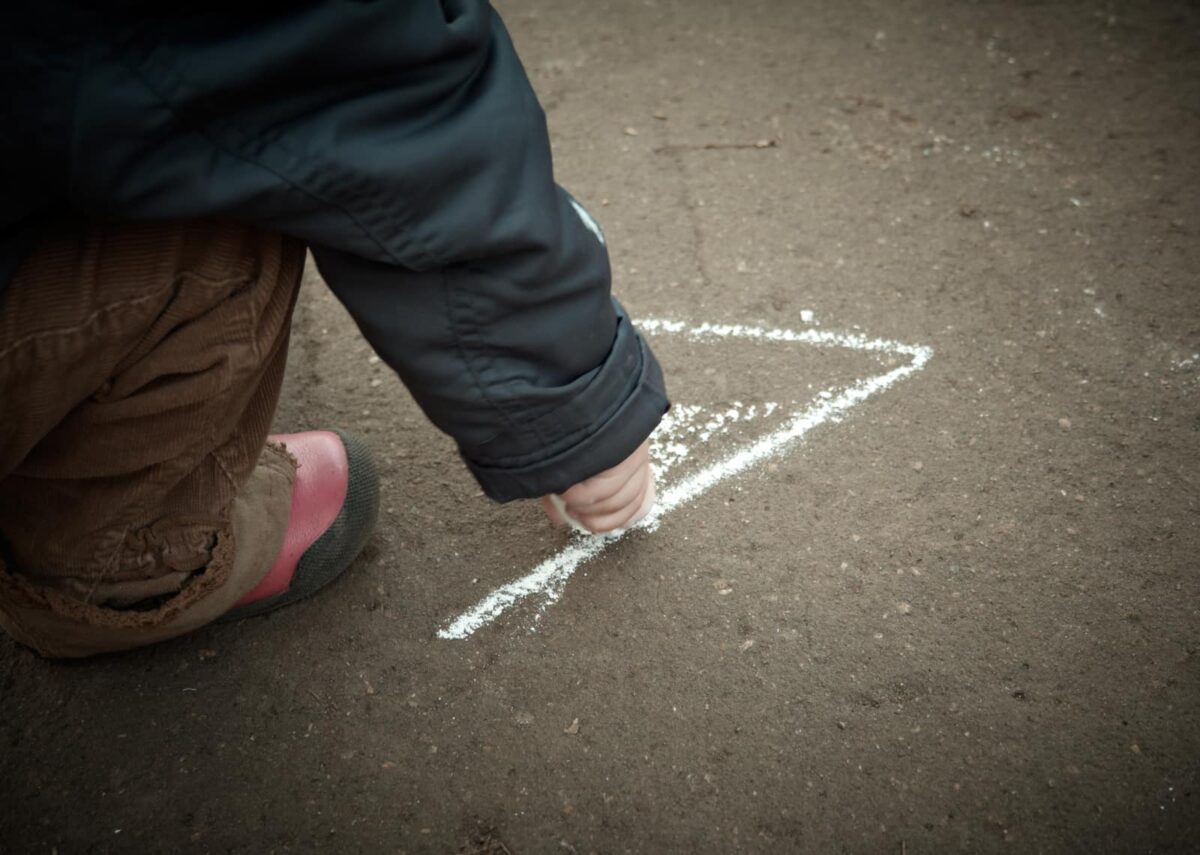 A young child writing with chalk on the sidewalk while outside playing. 