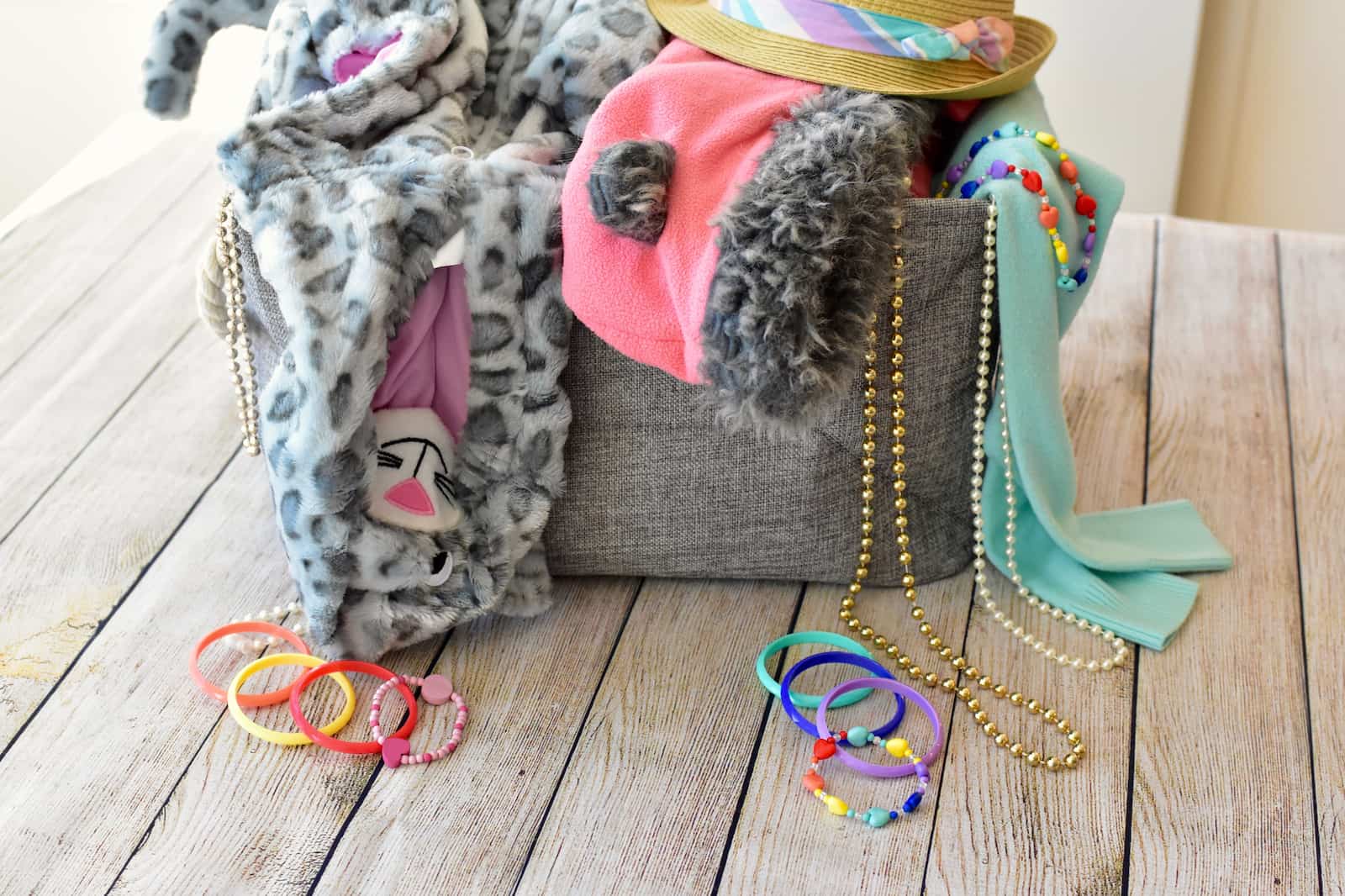 A gray bin that has fun dress up clothes overflowing from it. 
