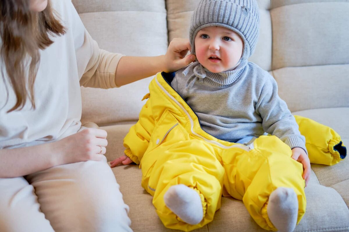 A young boy putting on a bright yellow snow suit. 