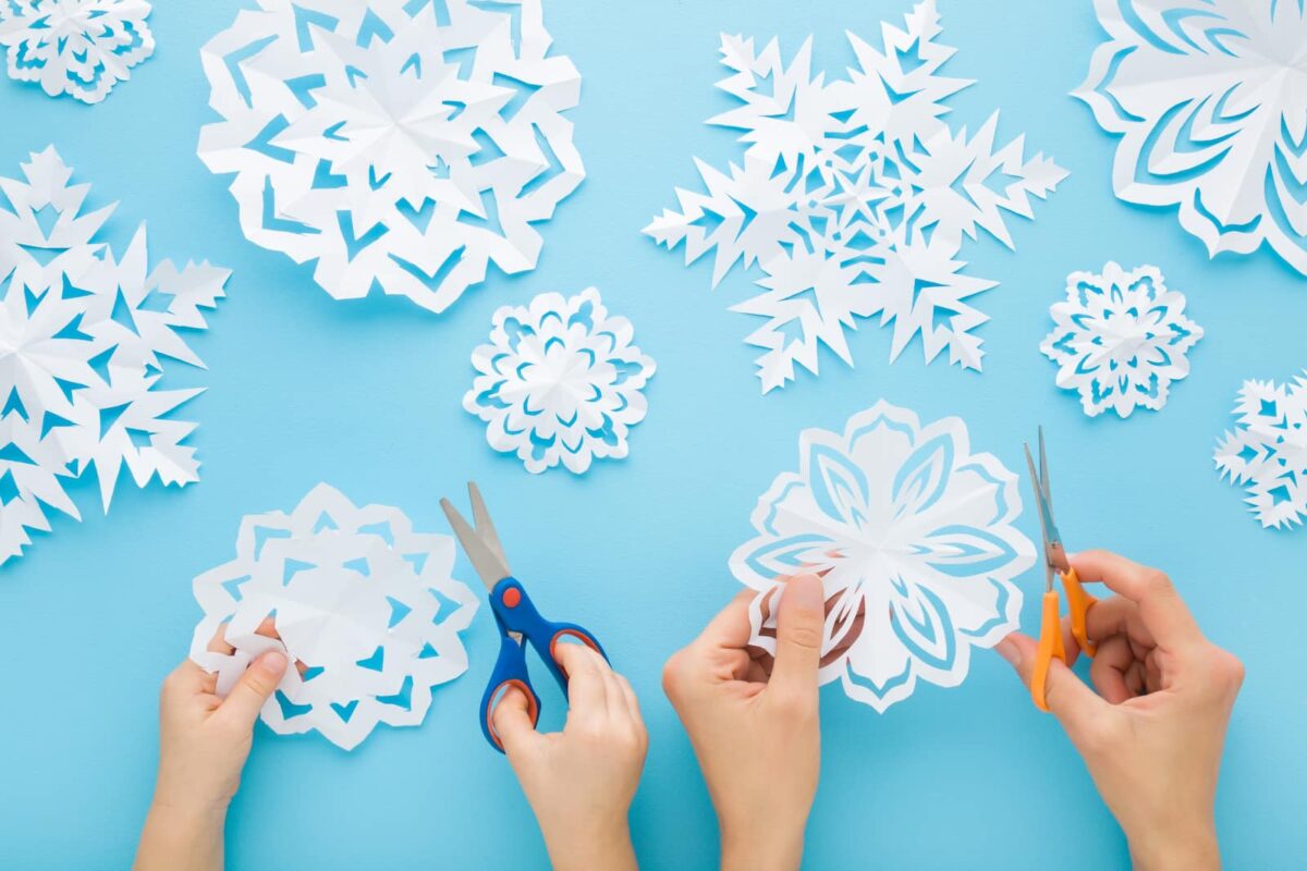 Intricate white snowflakes cut from white paper sitting on a light blue background. 