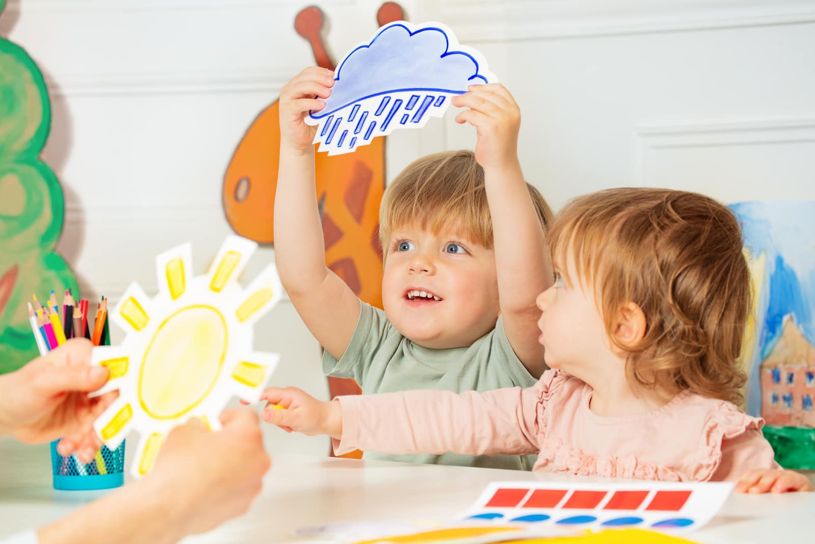 Preschoolers holding up pictures showing different weather patterns. 