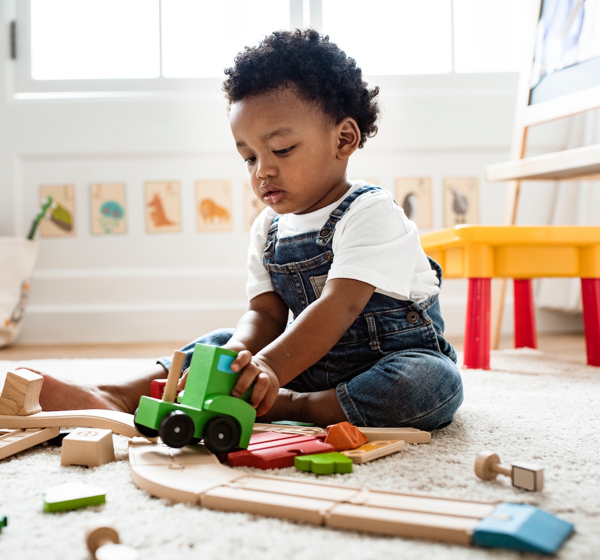 A young child playing with cars and blocks by himself in the middle of the floor. 
