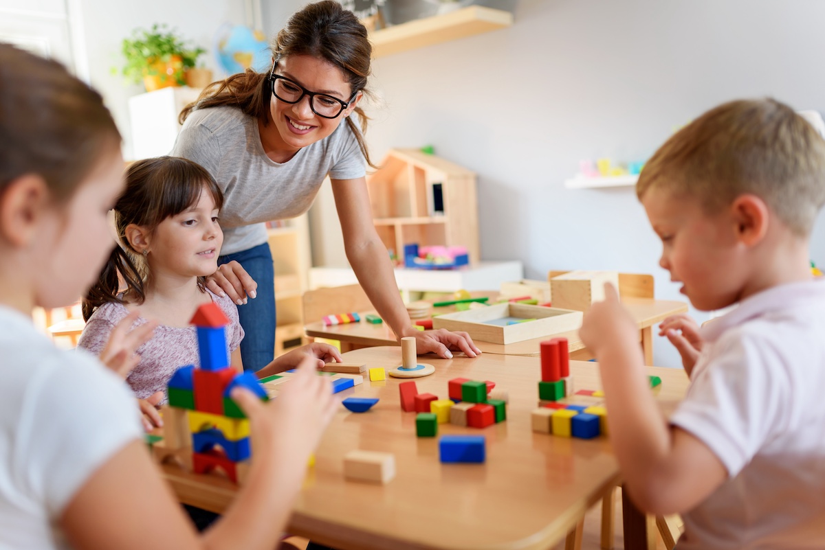 Children and teacher stacking colorful blocks together on a table in associative play. 