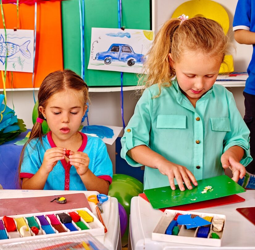 Two young girls playing with clay side by side in parallel play. 