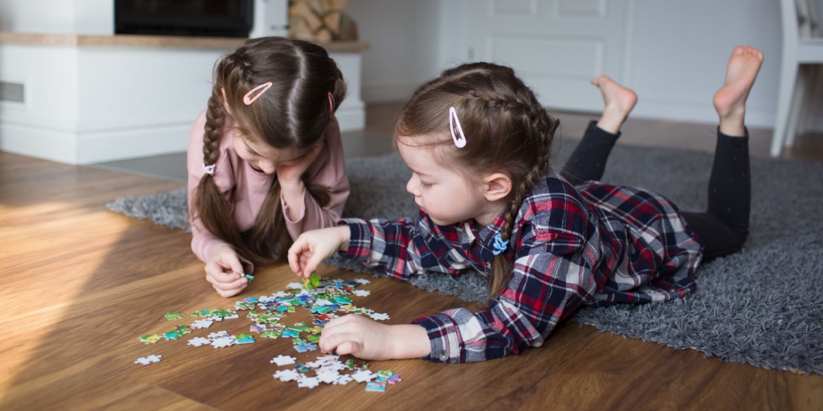 Two kids laying on the tummies on the floor playing with a puzzle. 
