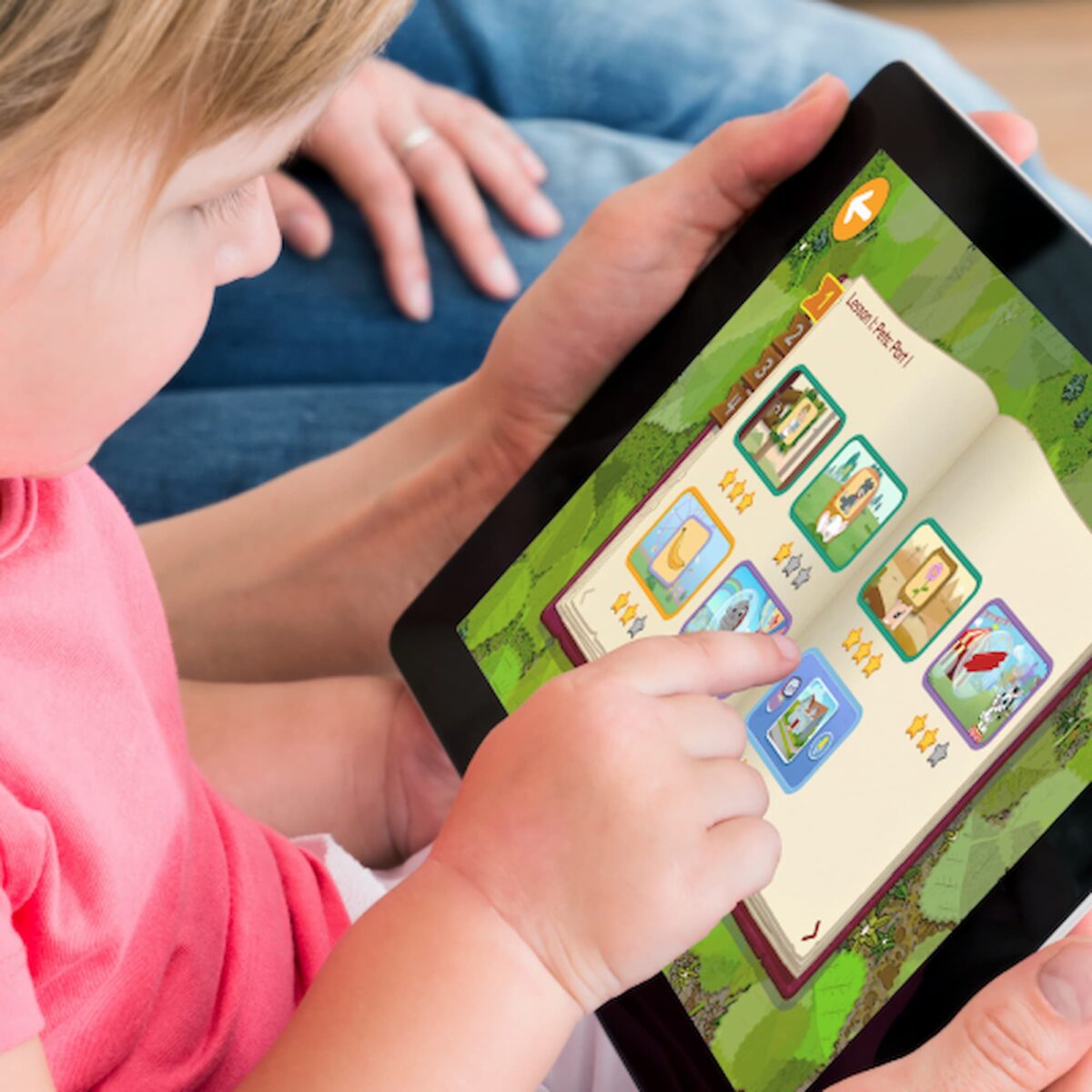 Young childe holding an i-pad in their lap playing on the ABCmouse education app. 