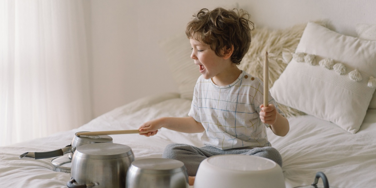 A young child playing drums on a bunch of kitchen pots and bowls. 