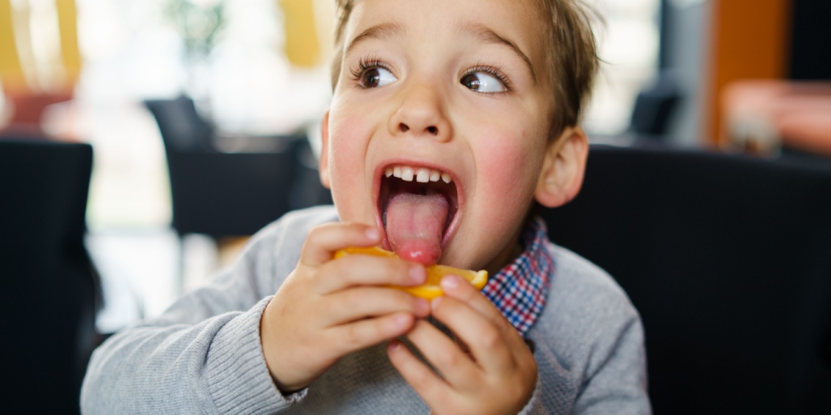A young kid licking an orange with a surprise face. 
