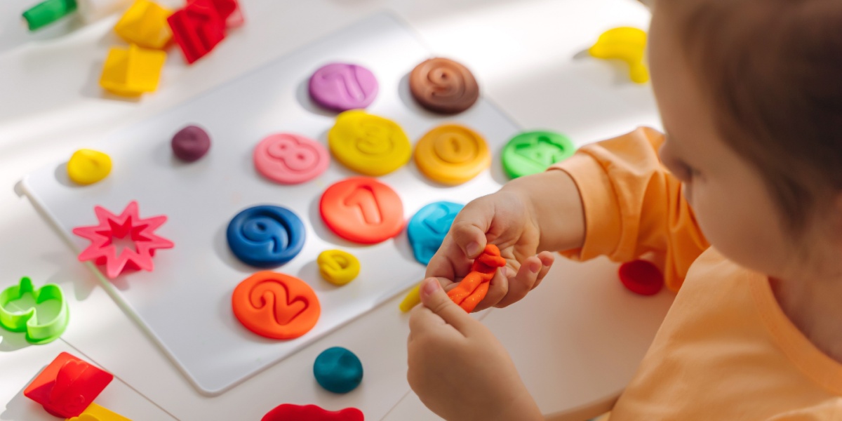 A young child playing with colorful playdough stamping numbers in it with cookie cutters. 