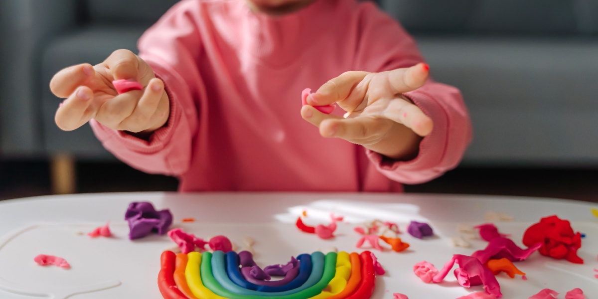 A child making a colorful rainbow from playdough in sensory play.