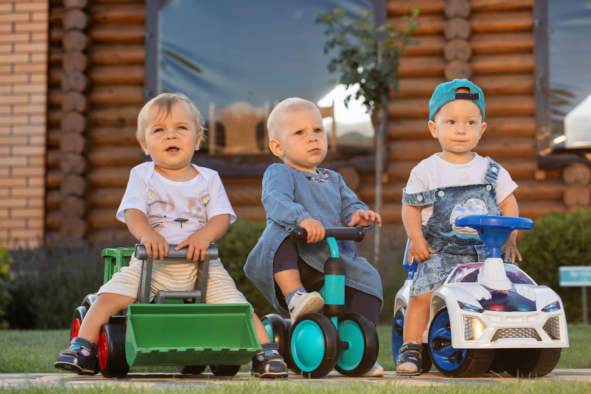 Three young boys sitting on ride-on toys outside in the yard. 