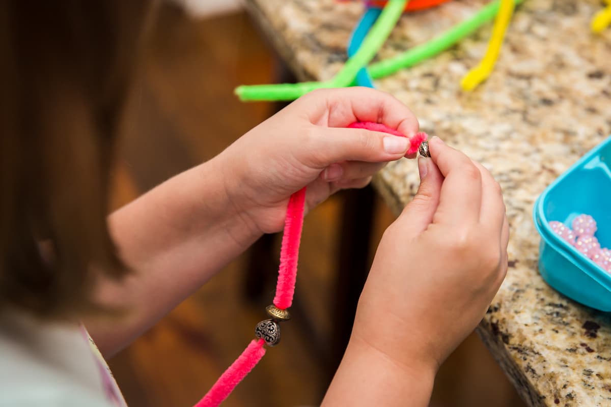 A young child's hands putting beads onto a pipe cleaner. 