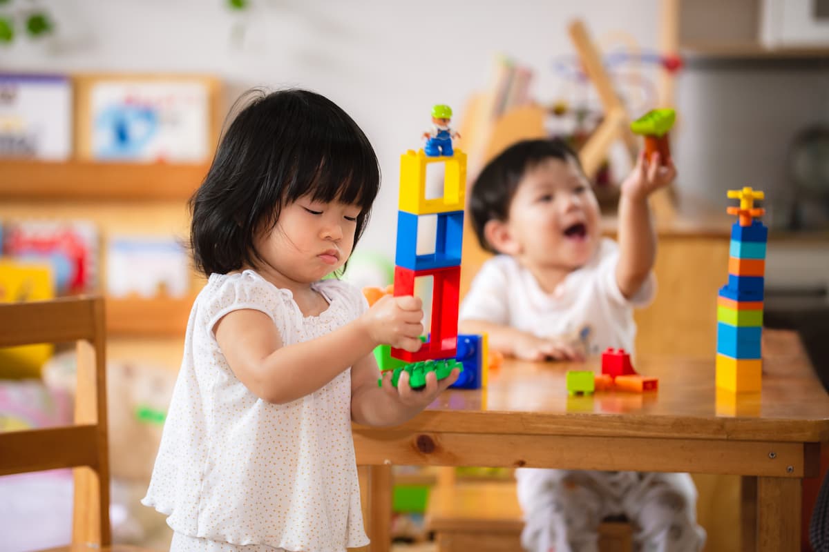 Two young children playing with blocks  at a table engaging in parallel play. 