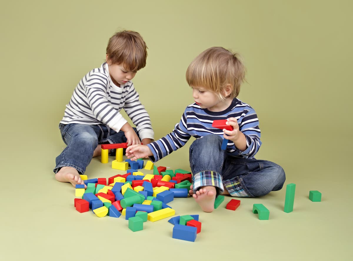 Two young boys playing with blocks on the floor engaging in solitary play. 