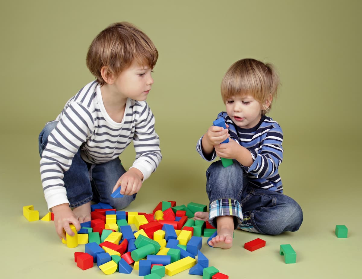 Two young boys playing with blocks on the floor engaging in parallel play. 