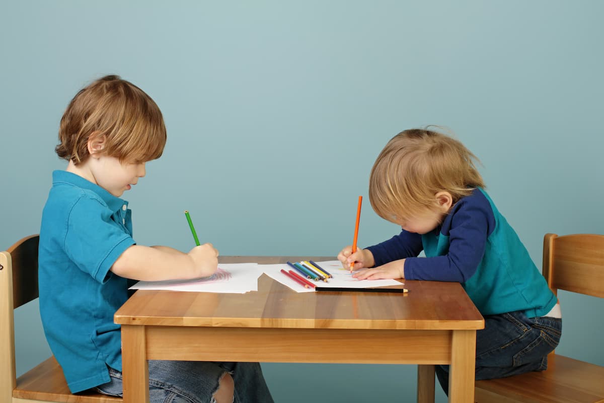 Two young boys sitting at a table engaging in parallel play. 