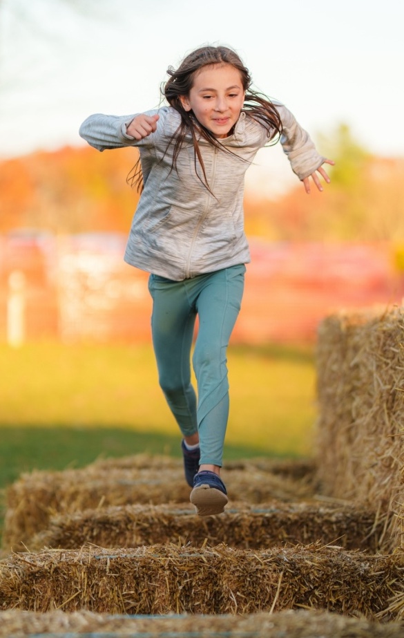 A young girl running across bales of hay in a fun fall themed obstacle course. 
