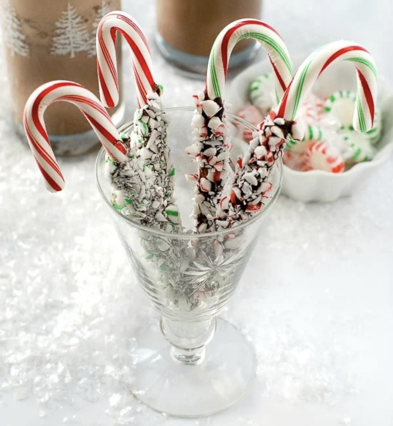 Chocolate dipped candy canes sitting in a fancy glass. 