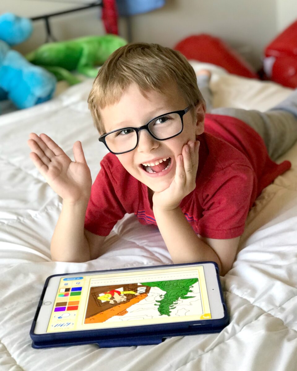 A young boy playing on the ABCmouse app on an i-pad waving hi to the camera. 
