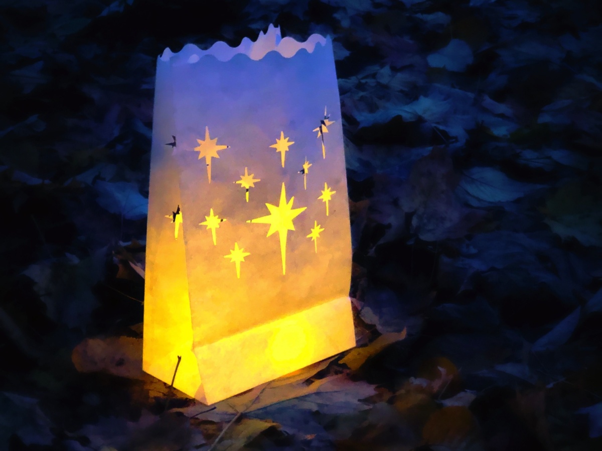 Glowing white paper sack with stars cut out as a homemade lantern craft for kids to make for Christmas. 