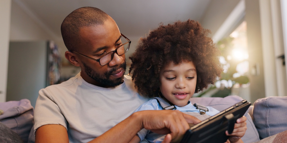 Father and daughter sitting together playing ABCmouse on a tablet.