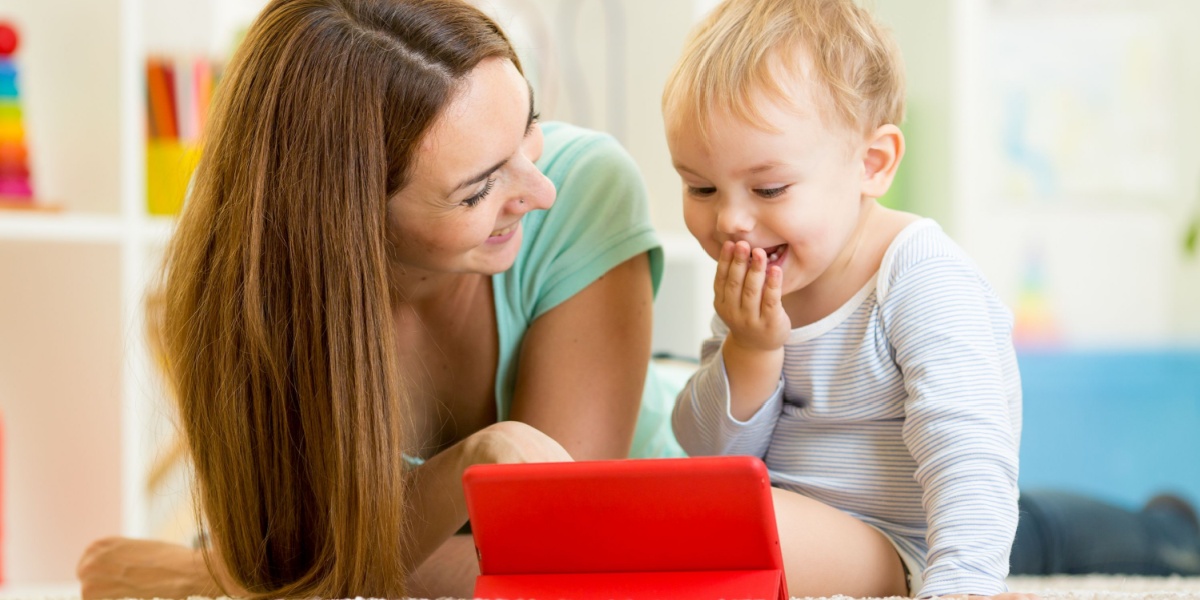 Mom and young child playing the ABCmouse app together on a bright red i-pad. 