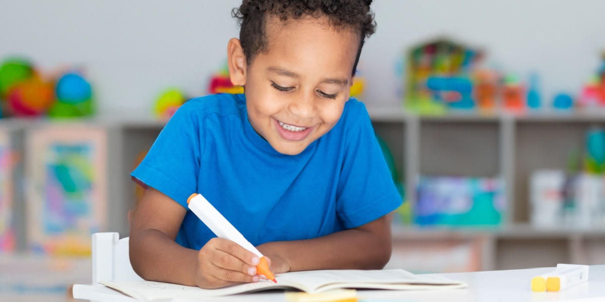 A young boy drawing in an art book for a fun door activity.