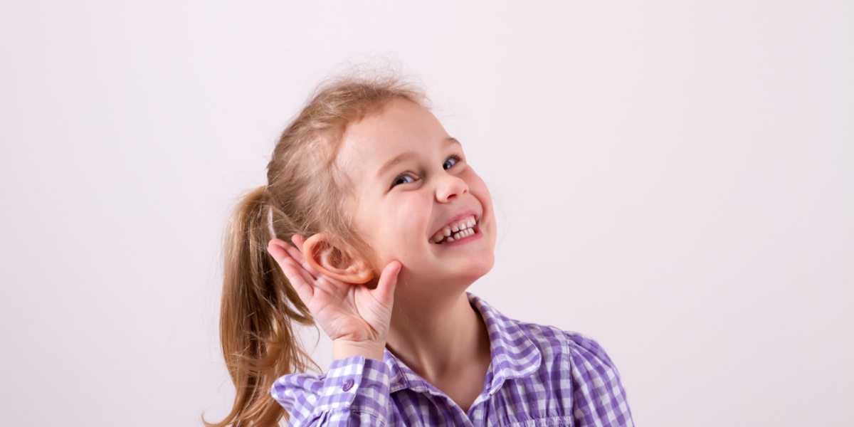 A young girl holding her hand to her ear with a big smile on her face.