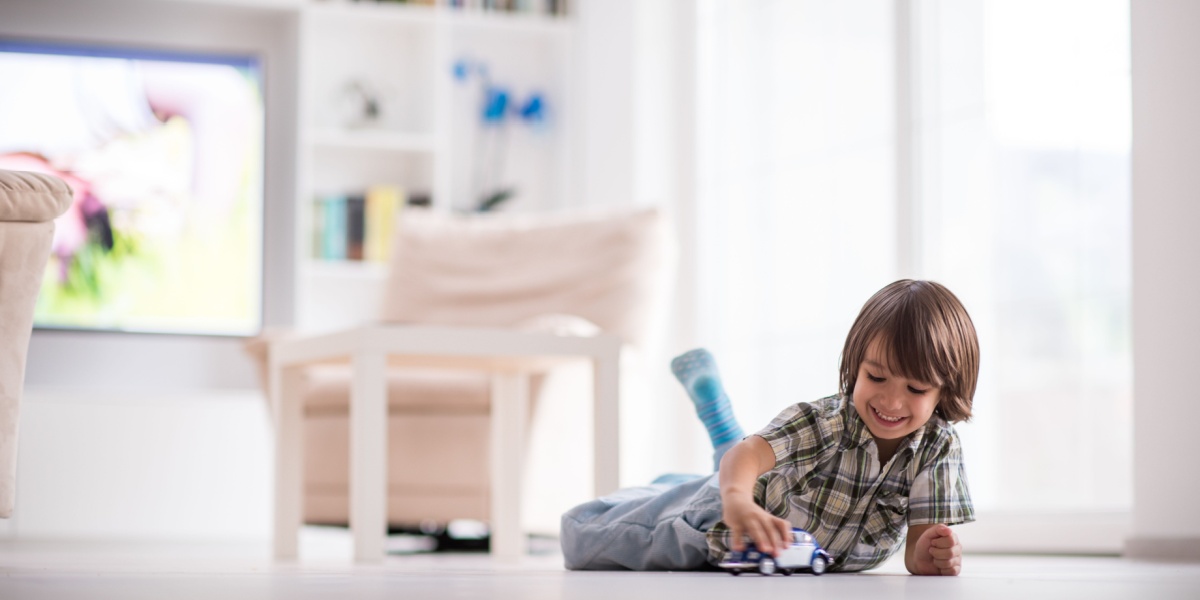 A young boy laying on his stomach on the floor playing with a toy truck.