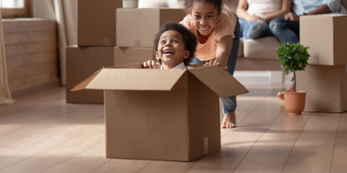 Young children playing indoors with empty carboard boxes.
