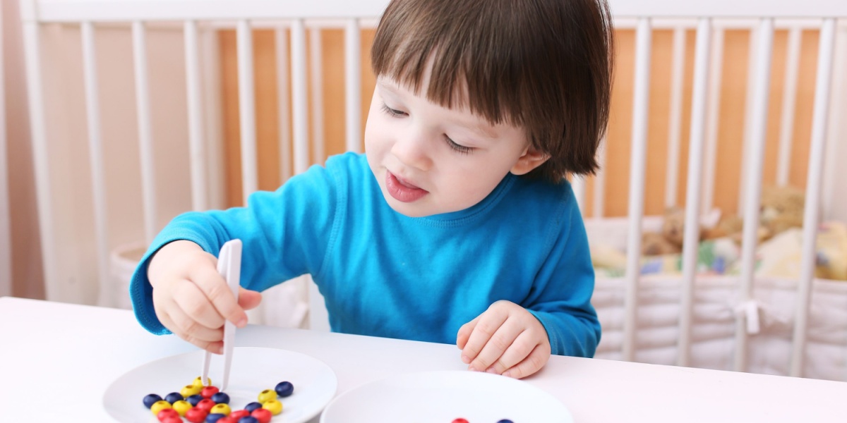 A young child using tweezers to transfer candies from one dish to another.