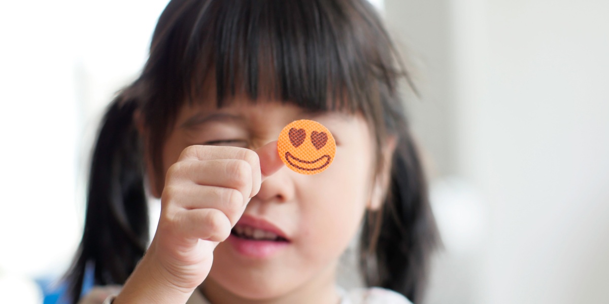 A cute little girl holding a smile face sticker on her thumb smiling in the background.