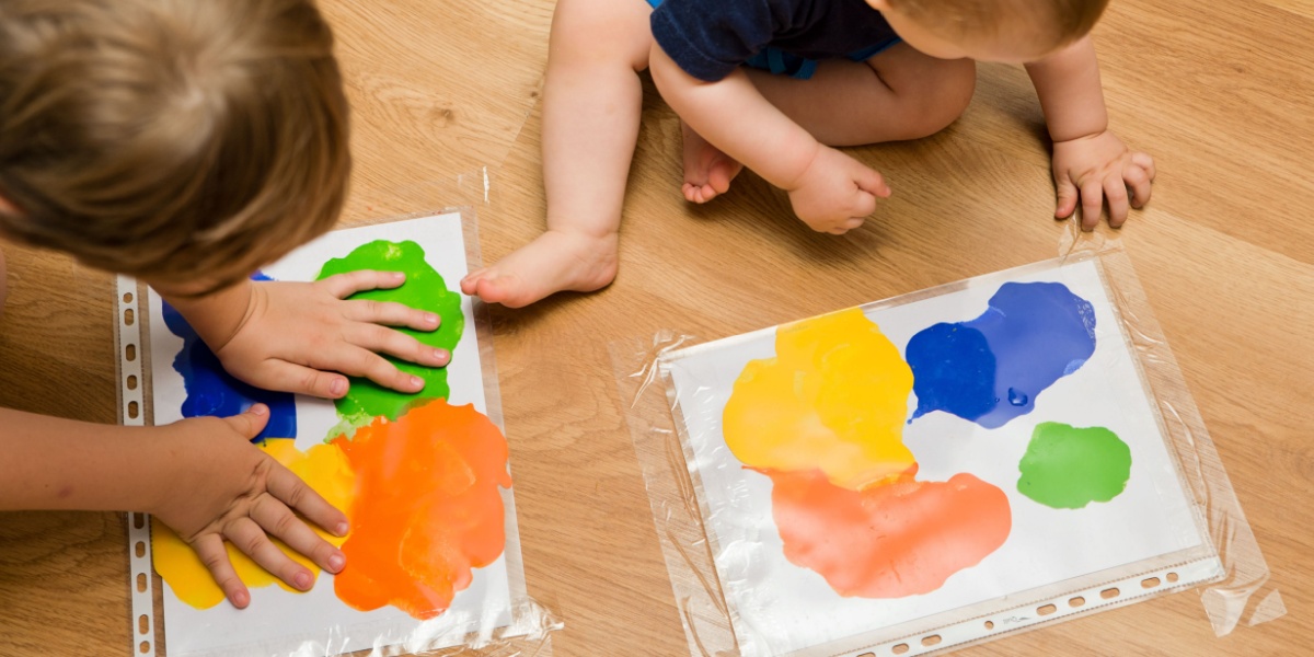 Young children pushing paint around a plastic sheet for a fun indoor learning activity.