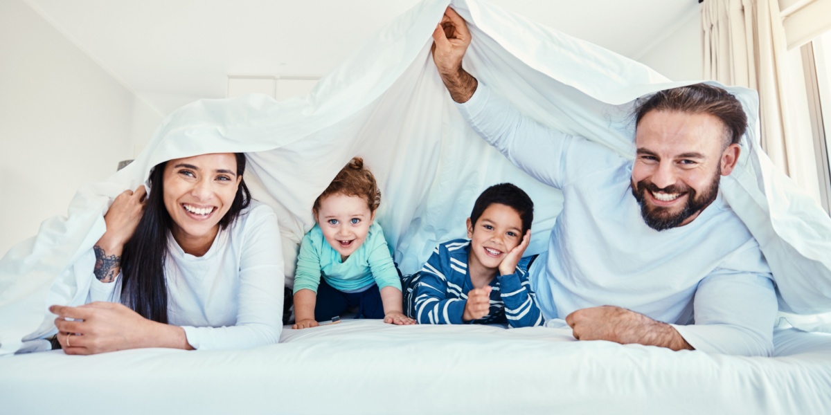 A young family playing together under a sheet on a bed.