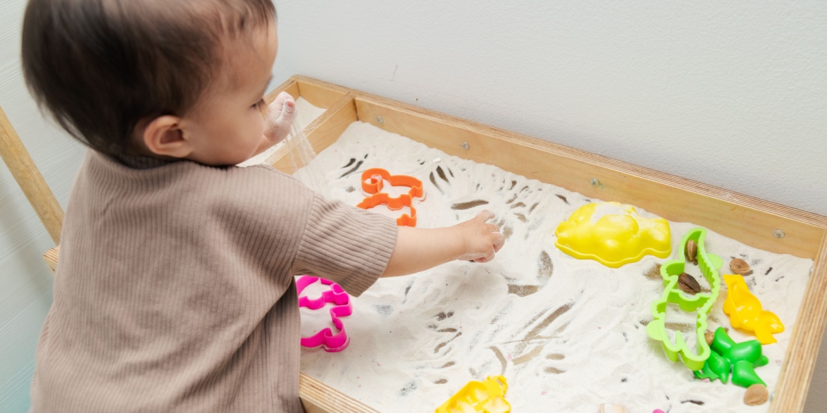 A young child playing in a sand tray with cookie cutters.