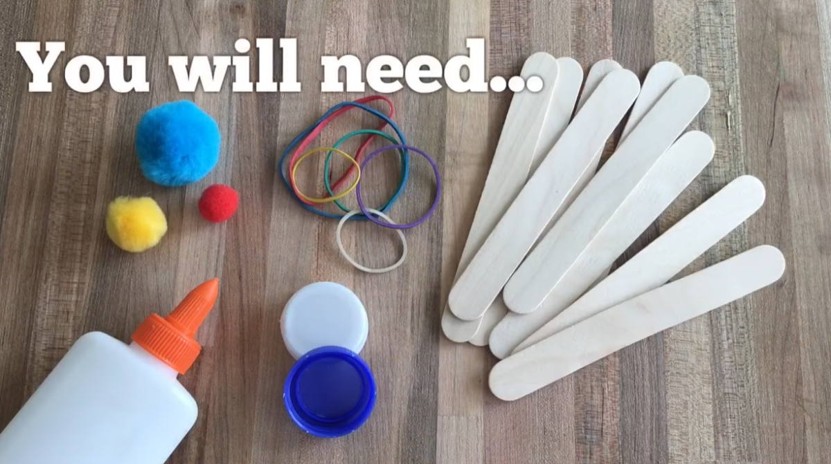 Materials needed to make a craft stick catapult, including craft sticks, rubber bands, glue, bottle caps, and pom-poms