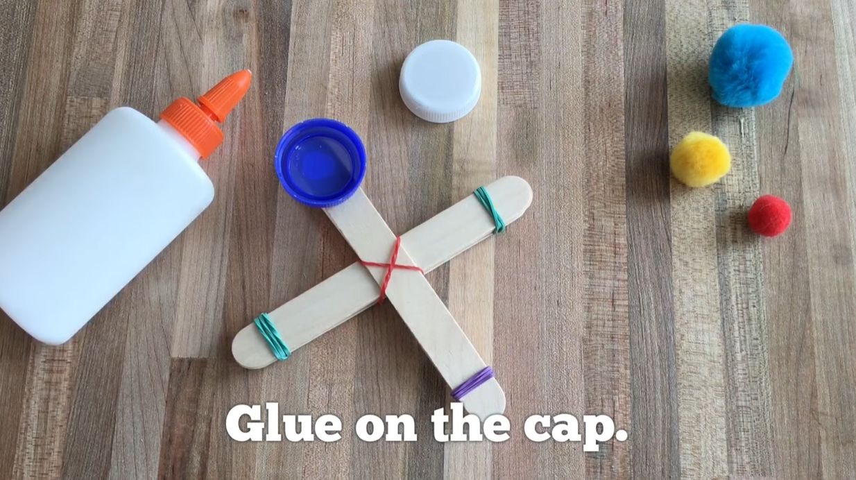 Gluing a plastic bottle cap onto the end of a craft stick catapult