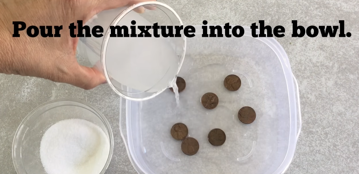 Pouring a vinegar and salt mixture over dirty pennies in a plastic container