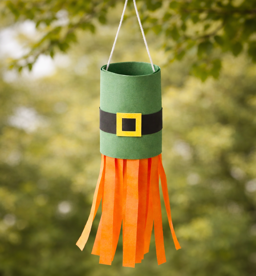 Hanging St. Patrick’s Day leprechaun craft made from a green paper tube with a black belt and yellow buckle, featuring orange paper streamers as a beard.