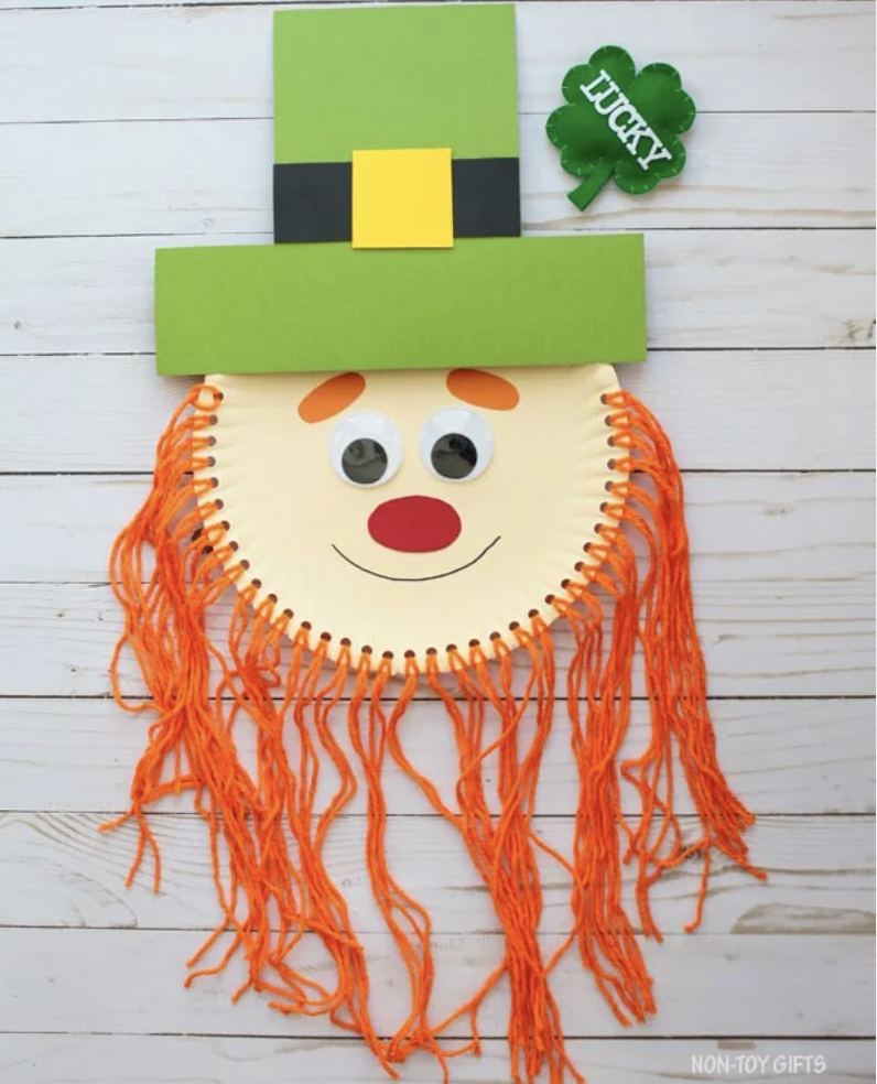 Paper plate leprechaun craft with googly eyes, a red nose, green hat, and long orange yarn beard hanging down.
