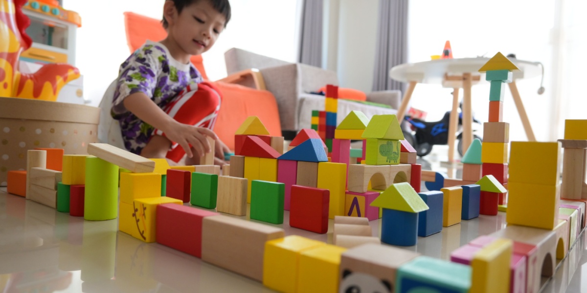 Young child playing with colorful wooden blocks and building structures on the floor.