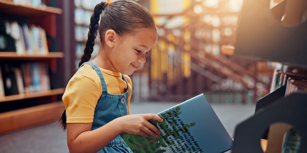 Young girl smiling while reading a book.