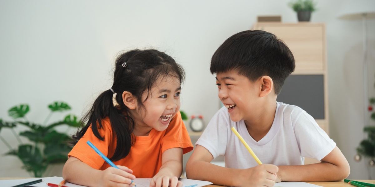 Two children laughing and drawing together at a table.