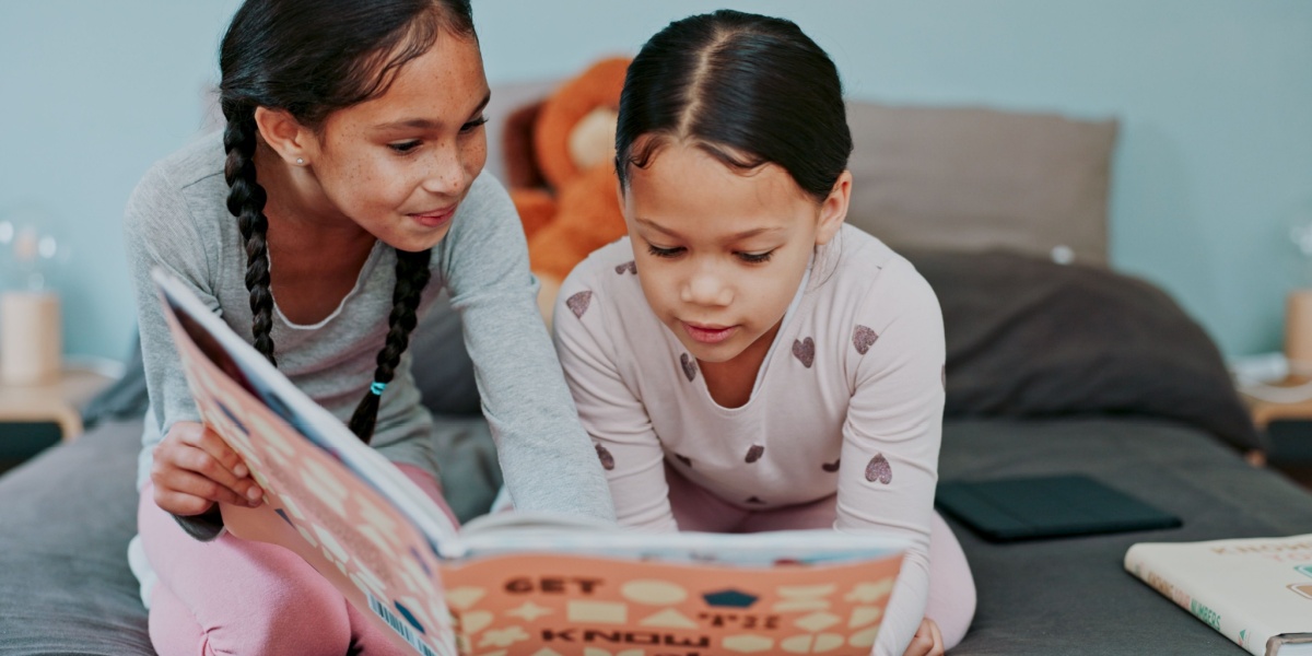Two young girls reading a book together